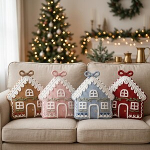 May include: Four house-shaped crochet cushions in brown, pink, blue, and red. Each cushion features white crocheted icing details, a central door, multiple windows, and a decorative bow at the top. The cushions are arranged side by side on a sofa.