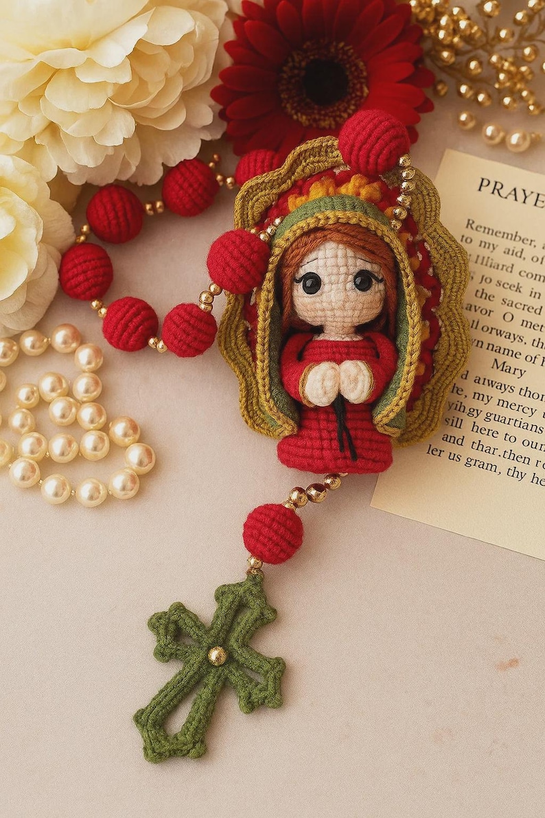 Puede incluir: Rosario de ganchillo hecho a mano con una mu&ntilde;eca vestida de rojo dentro de un marco dorado. El rosario incluye cuentas rojas, una cruz verde y detalles dorados. El fondo incluye flores y una tarjeta de oraci&oacute;n.