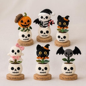 May include: Six crocheted Halloween figures in skull-shaped pots on wooden bases engraved with The Smith Family. Figures include a pumpkin, a skeleton, a black cat, a ghost with a pink bow, a black cat with an orange hat, and a grey bat.