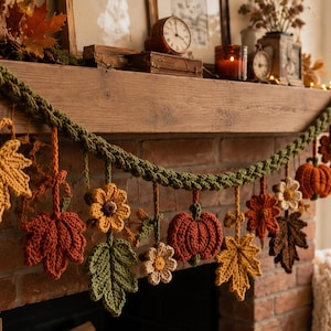 May include: A decorative garland featuring crocheted autumn elements including orange pumpkins, yellow and brown maple leaves, and small flowers suspended from a thick, braided olive green yarn cord, designed for seasonal home display.