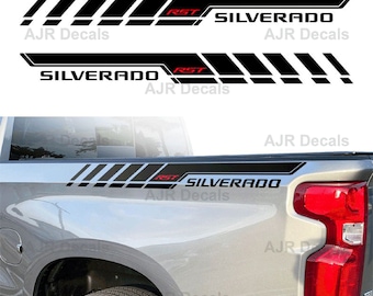 Puede incluir: Conjunto de calcomanías Silverado RST en negro y gris para una camioneta. Las calcomanías presentan las palabras "Silverado" y "RST" en letras blancas. Las calcomanías están diseñadas para ser aplicadas en el lateral de la caja de una camioneta.