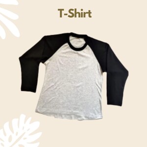 Puede incluir: Una camiseta de manga larga estilo b&eacute;isbol con torso gris jaspeado y mangas negras s&oacute;lidas con un cuello redondo negro a juego. El texto T-Shirt est&aacute; impreso en una fuente marr&oacute;n sin remates sobre la prenda en un fondo claro.
