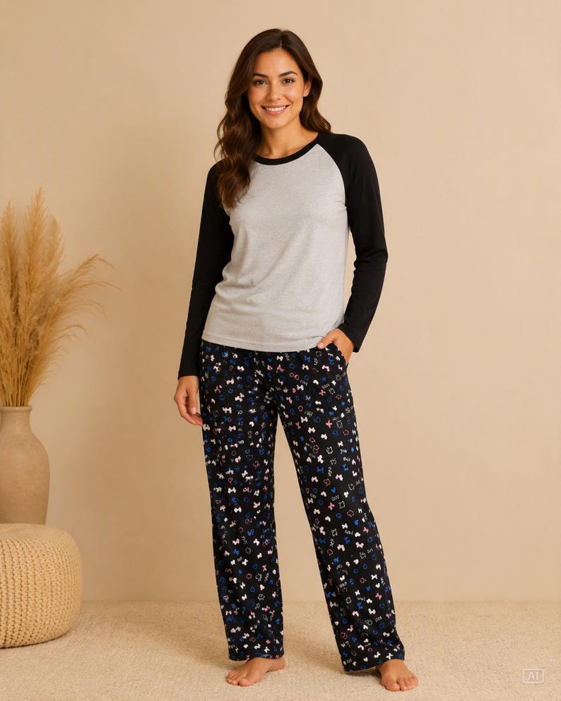 Puede incluir: Una camiseta de manga larga ragl&aacute;n con el torso gris jaspeado y mangas negras lisas, combinada con un pantal&oacute;n de pijama negro con un estampado repetitivo de peque&ntilde;os lazos y corazones coloridos en tonos rosa, azul y blanco por toda la tela.