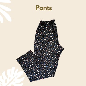 Puede incluir: Pantalones negros con un estampado de peque&ntilde;os lazos blancos, rosas y azules intercalados con la palabra "LOVE" en texto blanco. La prenda tiene una cintura el&aacute;stica fruncida y un corte de pierna recta sobre un fondo claro.