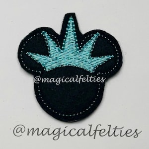 May include: Black felt applique in the shape of a mouse head with a turquoise crown. The applique has white stitching around the edges. The text "@magicalfelties" is written in a script font below and above the applique.