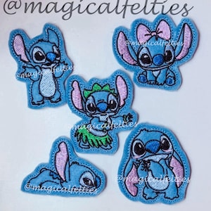 May include: A collection of five blue felt appliques featuring the character Stitch from Lilo & Stitch. Each applique has a different pose, with pink accents and embroidered details. The text "@magicalfelties" is present on each applique.