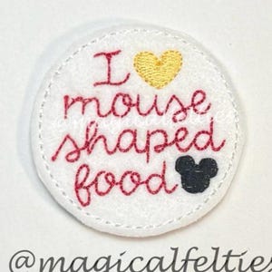 May include: A white felt patch with the embroidered phrase "I mouse shaped food" in red script. A yellow heart and a black mouse head are also embroidered on the patch. The text "@magicalfelties" is at the bottom.