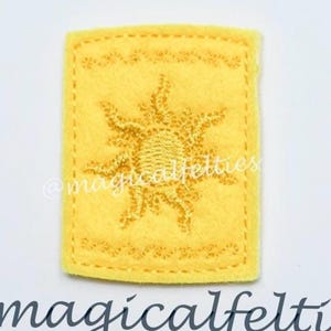 May include: A yellow felt patch with a sun design, featuring a decorative border and stitched details. The patch has the text "@magicalfelties" below it.