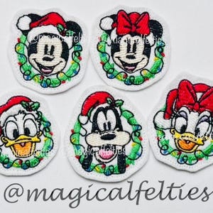 May include: Embroidered patches featuring Mickey Mouse, Minnie Mouse, Donald Duck, Goofy, and Daisy Duck, each wearing a Santa hat and surrounded by a Christmas wreath with lights. The text "@magicalfelties" is at the bottom.