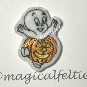 May include: An embroidered patch featuring a white ghost with black outlines emerging from a bright orange jack-o'-lantern with yellow eyes and a mouth. The design includes the text @magicalfelties embroidered in a cursive font across the center.
