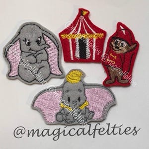 May include: Four felt appliques featuring characters and elements from a circus theme. Includes two gray elephants with pink accents, a red circus tent, and a red-clad character. The text "@magicalfelties" is visible.