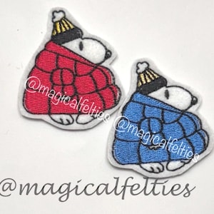 May include: Two felt Snoopy patches. One is red, the other is blue, both with a black and gold hat and a matching blanket. The patches have the text "@magicalfelties" in a cursive font.