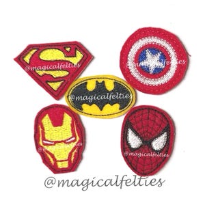 May include: Five embroidered fabric patches featuring superhero emblems and masks. The collection includes a red and yellow diamond-shaped logo, a circular red, white, and blue shield, a yellow oval with a black bat, a red and gold mask, and a red spider mask.