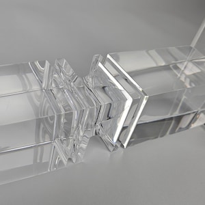 Può includere: Oggetto decorativo in acrilico trasparente con forme geometriche. L'oggetto è composto da blocchi rettangolari e quadrati, con una superficie riflettente. Il design presenta una serie di elementi trasparenti impilati, creando un'estetica moderna.