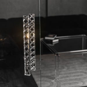 May include: A clear glass door handle with a geometric pattern. The handle is attached to a glass door.