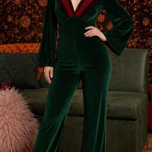 Può includere: Tuta in velluto verde scuro con maniche lunghe svasate e gamba larga. Lo scollo a V presenta una striscia bordeaux a contrasto. La tuta è un capo unico.