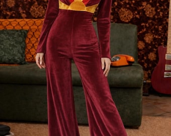 May include: Burgundy velvet jumpsuit with long sleeves and flared legs. The neckline features a V-shape with a gold, red, and yellow design. The jumpsuit is a retro style, suitable for parties and special events.