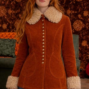 May include: Rust-colored corduroy jacket with a cream-colored faux fur collar and cuffs. The jacket features a row of gold buttons down the front and two large front pockets. A stylish outerwear piece.