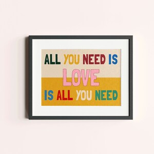 May include: A framed print with the text "ALL YOU NEED IS LOVE IS ALL YOU NEED" in colorful letters on a yellow and beige background.
