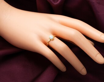 Puede incluir: Un anillo de oro con una piedra ovalada blanca. El anillo está en una mano de maniquí.