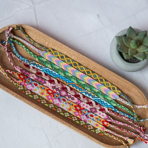 Bracelets brésilien colorés dans un plateau en bois sur un table en pierre avec un succulent. Bracelets d'amitié dans un style coloré, boho et hippie.