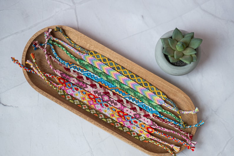 Bracelets brésilien colorés dans un plateau en bois sur un table en pierre avec un succulent. Bracelets d'amitié dans un style coloré, boho et hippie.