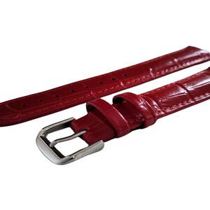 K&ouml;nnte beinhalten: Ein Paar rote Uhrenarmb&auml;nder mit gl&auml;nzendem Finish und Krokodilleder-Textur. Ein Armband hat eine silberne Schnalle. Die Armb&auml;nder sind zur Befestigung an einem Zifferblatt konzipiert. Die Armb&auml;nder sind neu.