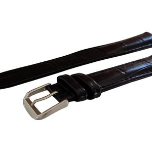 K&ouml;nnte beinhalten: Schwarzes Uhrenarmband mit strukturiertem Muster im Krokodil-Stil. Das Armband hat eine silberfarbene Schnalle und ist f&uuml;r den Anschluss an ein Zifferblatt konzipiert. Das Armband besteht aus flexiblem Material.