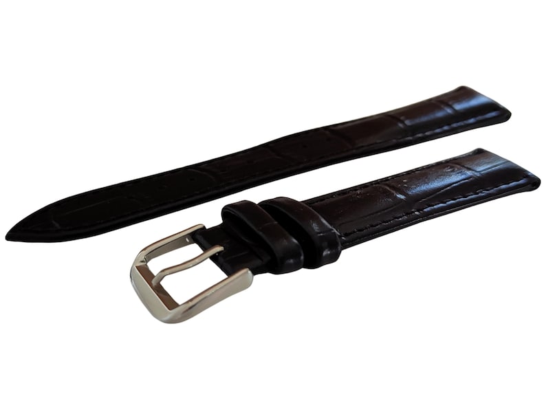 K&ouml;nnte beinhalten: Schwarzes Uhrenarmband mit strukturiertem Muster im Krokodil-Stil. Das Armband hat eine silberfarbene Schnalle und ist f&uuml;r den Anschluss an ein Zifferblatt konzipiert. Das Armband besteht aus flexiblem Material.
