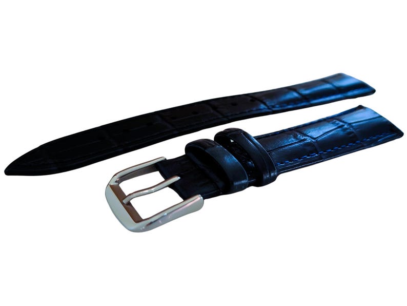 K&ouml;nnte beinhalten: Ein schwarzes Uhrenarmband mit einem strukturierten, krokodilartigen Muster. Das Armband verf&uuml;gt &uuml;ber eine silberfarbene Schnalle und ist zur Befestigung an einem Zifferblatt konzipiert. Das Armband besteht aus einem strapazierf&auml;higen Material.