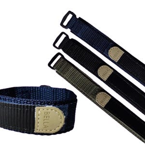 Puede incluir: Tres correas de reloj ajustables en negro, gris oscuro y verde oliva con la palabra "BELLA" impresa en cada correa.