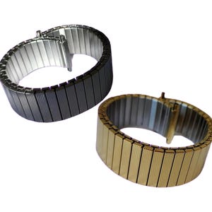 Op de afbeelding: Twee metalen horlogebandjes, een zwart en een gouden, met een schakellink-ontwerp.