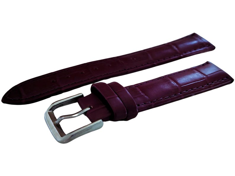 K&ouml;nnte beinhalten: Ein burgunderfarbenes Lederarmband mit einer silberfarbenen Schnalle. Das Armband hat ein strukturiertes, krokodilartiges Muster. Das Uhrenarmband wird vor einem wei&szlig;en Hintergrund gezeigt.