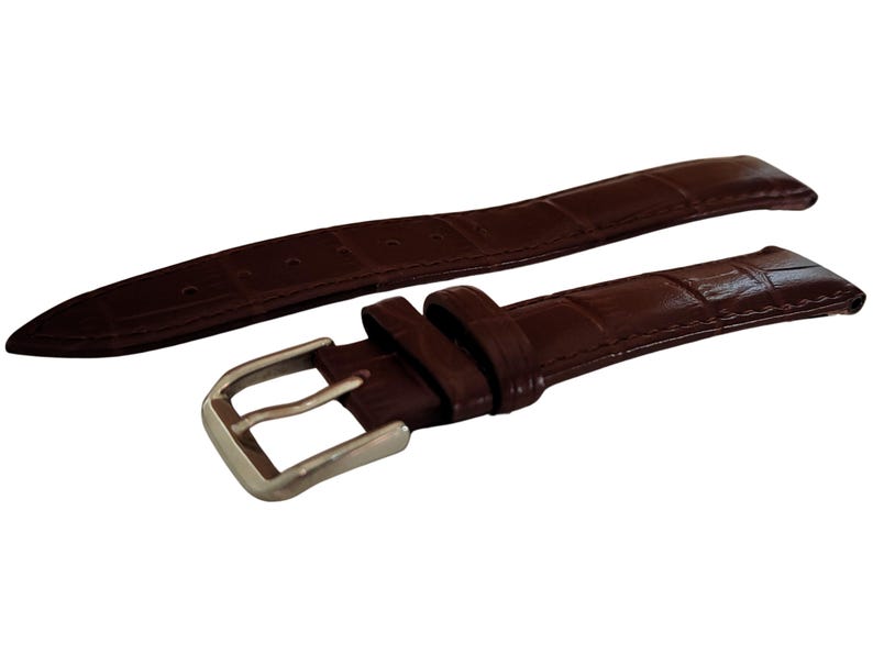 K&ouml;nnte beinhalten: Ein braunes Uhrenarmband mit einem strukturierten, krokodilartigen Muster. Das Armband ist in zwei Teile geteilt, mit einer silberfarbenen Schnalle an einem Ende. Das Leder hat eine satte, dunkelbraune Farbe.