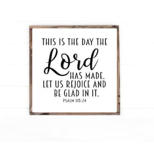 May include: A white wooden sign with a black inscription that reads "This is the day the Lord has made. Let us rejoice and be glad in it. Psalm 118:24".