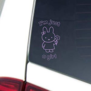 May include: A pink vinyl decal featuring a cartoon bunny holding a flower. The text "I'm just a girl" is above and below the bunny. The decal is applied to a car window.