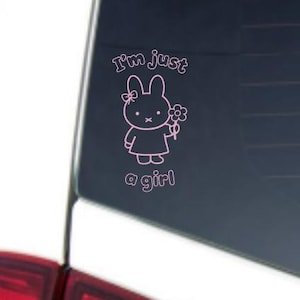 May include: Pink vinyl decal featuring a cartoon bunny holding a flower. The text "I'm just a girl" is above and below the bunny. The decal is applied to a car window.
