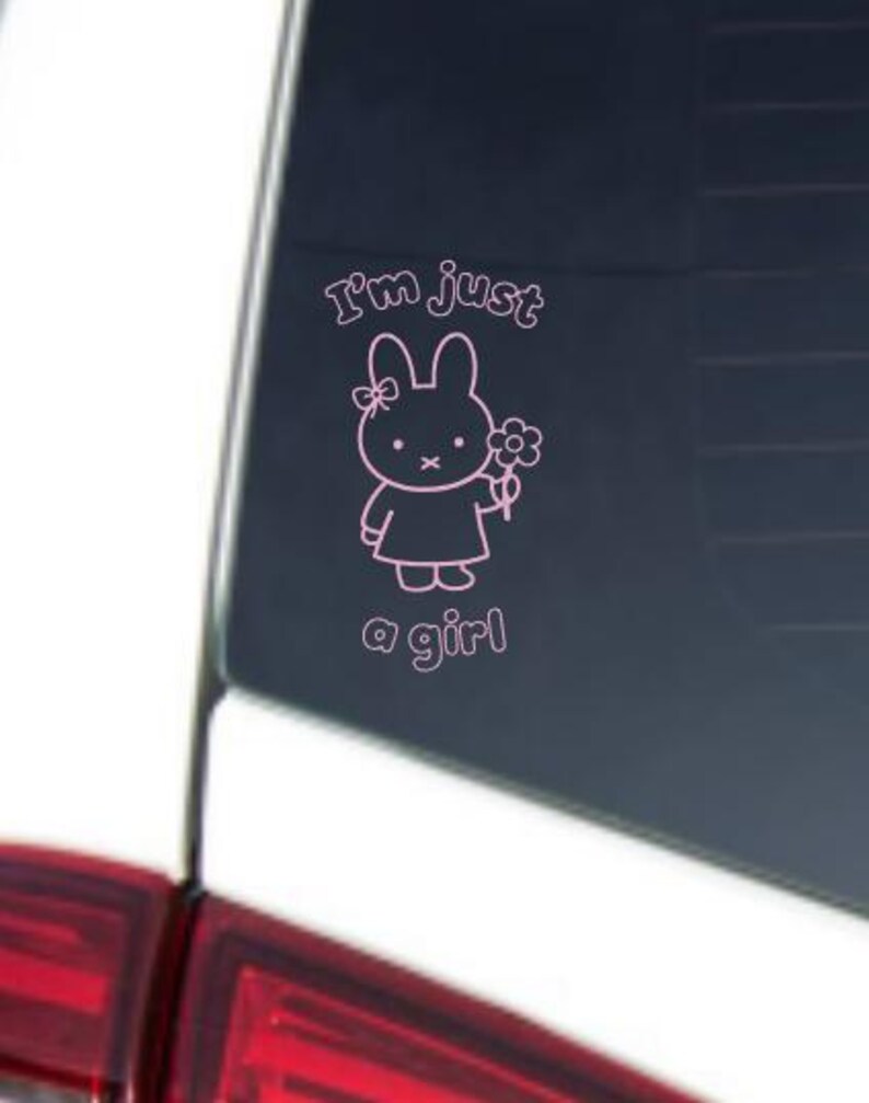 May include: Pink vinyl decal featuring a cartoon bunny holding a flower. The text "I'm just a girl" is above and below the bunny. The decal is applied to a car window.