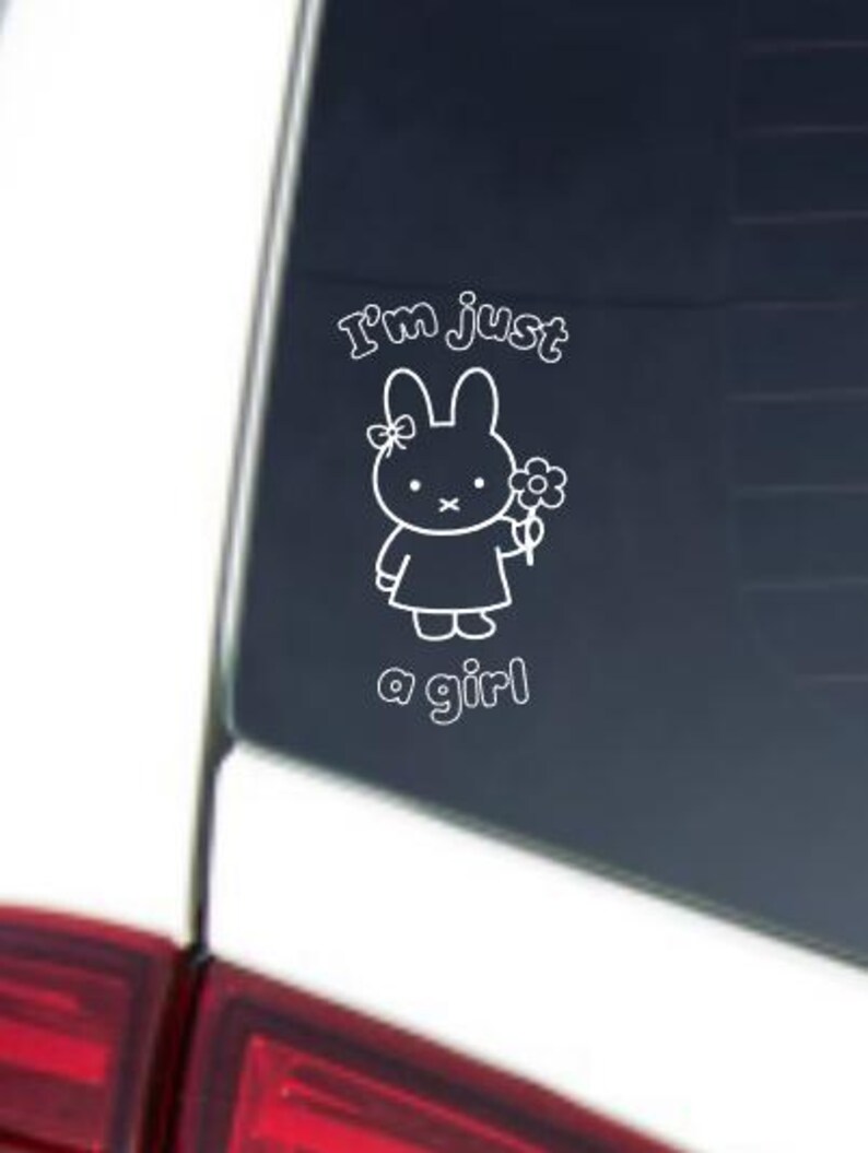 May include: White vinyl decal featuring a cartoon bunny holding a flower, with the text "I'm just a girl". The bunny has a bow on its head and is wearing a dress. The decal is likely for a car window or similar surface.