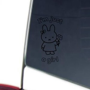 May include: Black and white decal featuring a cartoon bunny holding a flower. The text "I'm just a girl" is above and below the bunny illustration. The decal is applied to a car window.