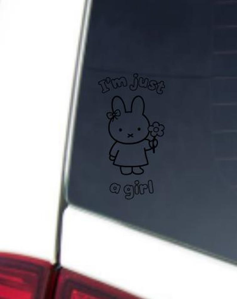 May include: Black and white decal featuring a cartoon bunny holding a flower. The text "I'm just a girl" is above and below the bunny illustration. The decal is applied to a car window.