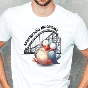 Op de afbeelding: Wit T-shirt met een cartoonvogel op een achtbaan. De tekst op het shirt luidt "Ich bin nur drolf mal gefahren".