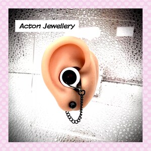 May include: Black chain earring with a white and black ear cuff. The earring is attached to the ear cuff with a small black bead. The ear cuff is worn on a model ear.