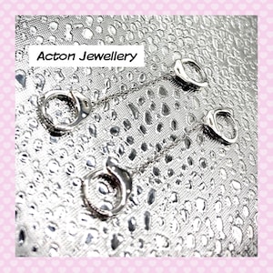May include: A silver jewellery set comprising two pendant necklaces and a pair of earrings. Each piece features a circular design with a chain. The text "Acton Jewellery" is displayed in a white box.