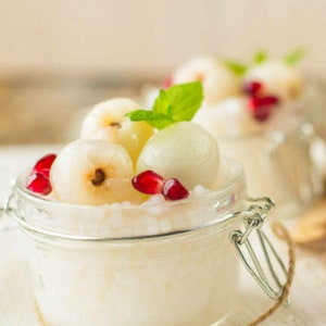 May include: A glass jar filled with white tapioca pudding topped with lychees and pomegranate seeds.