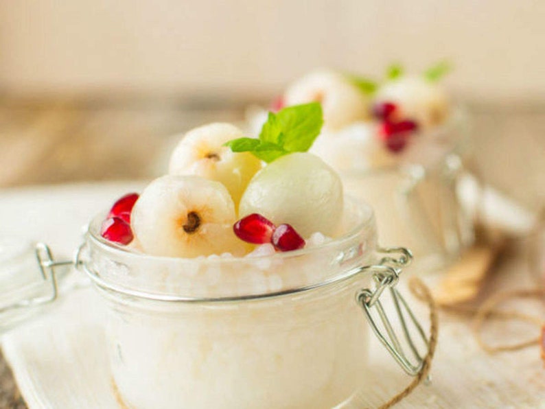 May include: A glass jar filled with white tapioca pudding topped with lychees and pomegranate seeds.
