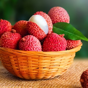 May include: A wicker basket filled with fresh lychees, some with the skin removed, revealing the white flesh. The basket is on a hessian surface.