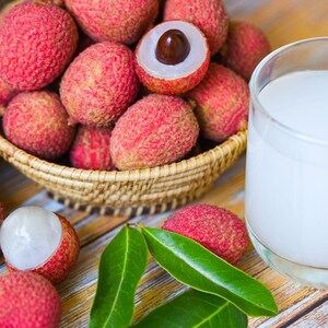 May include: A glass of lychee juice next to a bowl of fresh lychees. The lychees are pink and have a rough texture. The juice is white and opaque.