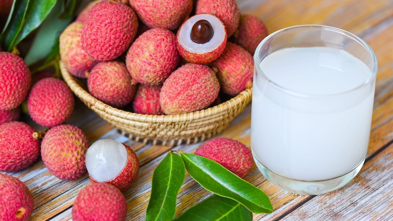 May include: A glass of lychee juice next to a bowl of fresh lychees. The lychees are pink and have a rough texture. The juice is white and opaque.