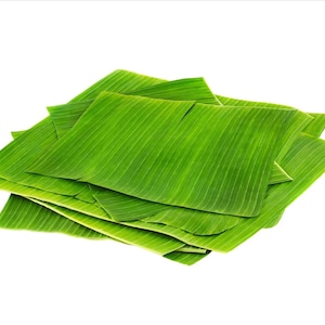 May include: A stack of green banana leaves, folded and arranged in a neat pile. The leaves are smooth and have a slightly glossy texture.